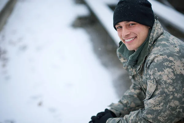 Hace frío, pero sigo comprometido. Un disparo de un joven soldado sentado afuera en un día nevado. — Foto de Stock