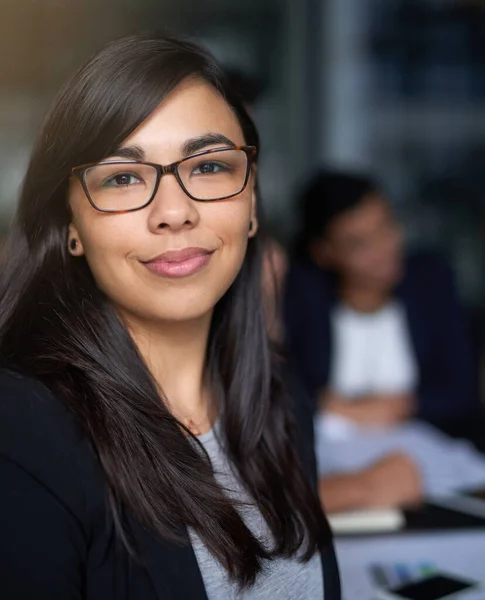 Hon är en tillgång för företaget. Porträtt av en leende ung affärskvinna på ett kontor med kollegor i bakgrunden. — Stockfoto