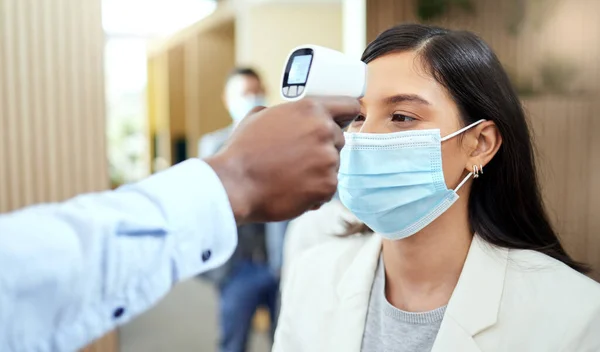 Lets take your temperature. Cropped shot of an attractive young businesswoman wearing a mask and having her temperature taken while standing at the head of a queue in her office. — Stock Photo, Image
