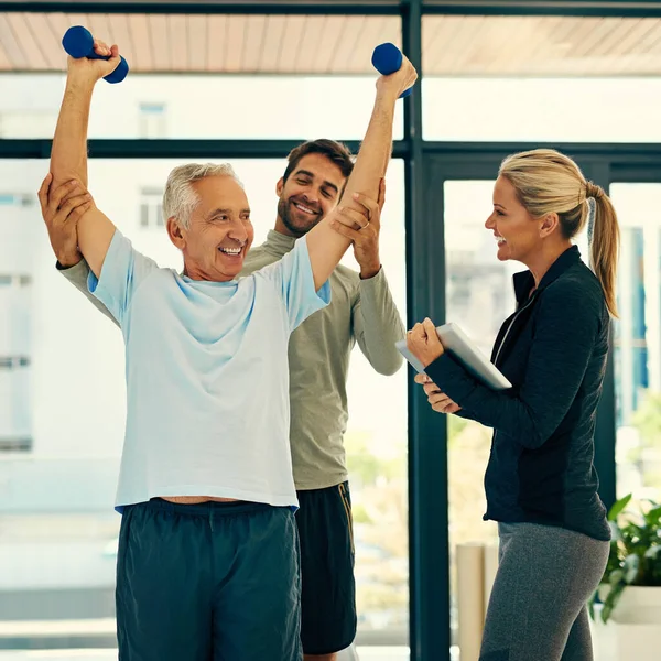 Er ist ihr Lieblingspatient. Aufnahme von zwei Physiotherapeuten, die ihrem älteren Patienten bei seinen Übungen helfen. — Stockfoto