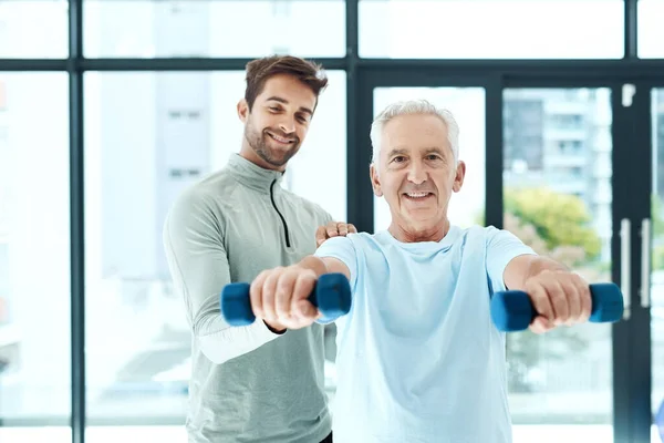 Sicher stärker, als man denkt. Aufnahme eines freundlichen Physiotherapeuten, der seinem älteren Patienten beim Training mit Gewichten hilft. — Stockfoto