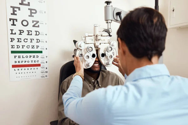 Всегда стоит сходить к оптометристу. Снимок оптометриста, осматривающего глаза пациентов оптическим рефрактором. — стоковое фото