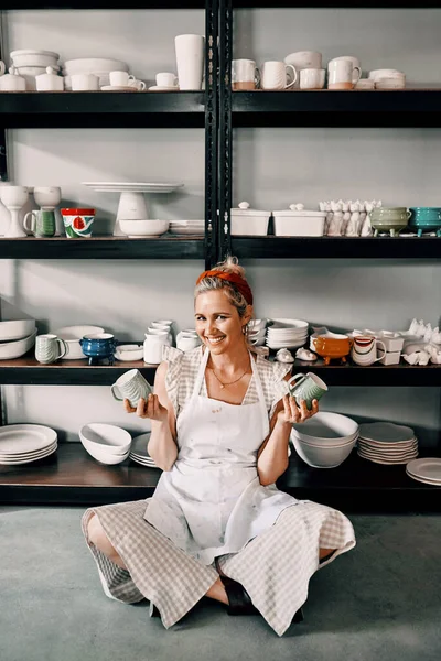 Escoge tú. Retrato de larga duración de una atractiva mujer madura sentada en el suelo y sosteniendo su cerámica en su taller. —  Fotos de Stock