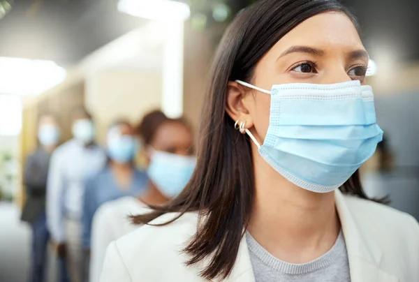 Det säkra sättet att arbeta. Beskuren bild av en attraktiv ung affärskvinna klädd i en mask när hon står i kö på sitt kontor. — Stockfoto