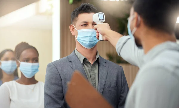 Lined up to be screened. Cropped shot of a handsome mature businessman wearing a mask and having his temperature taken while standing at the head of a queue in his office. — Stock Photo, Image