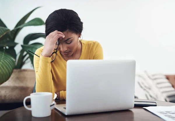 To nie idzie za dobrze. Strzał atrakcyjnej młodej kobiety siedzącej samotnie w domu i cierpiącej na ból głowy podczas korzystania z laptopa. — Zdjęcie stockowe