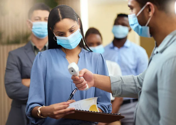 Your temperature looks good. Cropped shot of an attractive young businesswoman wearing a mask and going through covid screen while standing at the head of a queue in her office. — Stock Photo, Image