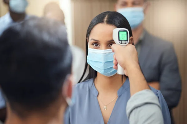 Let me just get your temperature. Cropped shot of an attractive young businesswoman wearing a mask and having her temperature taken while standing at the head of a queue in her office. — Stock Photo, Image