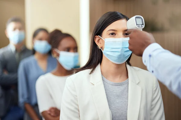 Getting their temperatures taken. Cropped shot of an attractive young businesswoman wearing a mask and having her temperature taken while standing at the head of a queue in her office. — Stock Photo, Image