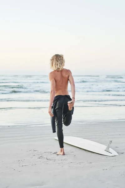 Rozciągam się, zanim uderzę w fale. Zdjęcie z tyłu młodego mężczyzny rozciągającego się przed pójściem surfować na plaży. — Zdjęcie stockowe
