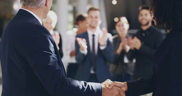 Hard werken wordt nooit onherkend. 4k videobeelden van twee zakenmensen schudden handen in een kantoor met collega 's applaudisseren op de achtergrond. — Stockfoto