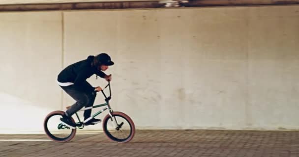 De stedelijke jungle temmen. 4k video van een jonge bmx fietser doet trucs op zijn fiets onder een brug. — Stockvideo