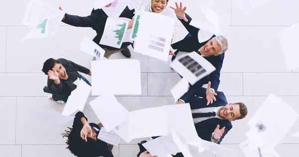 Закончили на сегодня. Аэросъемка разнообразной группы бизнесменов, швыряющих бумажную работу в воздух во время празднования в офисе. — стоковое фото