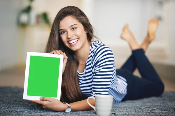 Die beste Seite, die Sie jemals finden werden. Porträt einer lächelnden jungen Frau, die zu Hause auf dem Boden liegt und ein digitales Tablet mit einem Chroma-Keyscreen hochhält. — Stockfoto