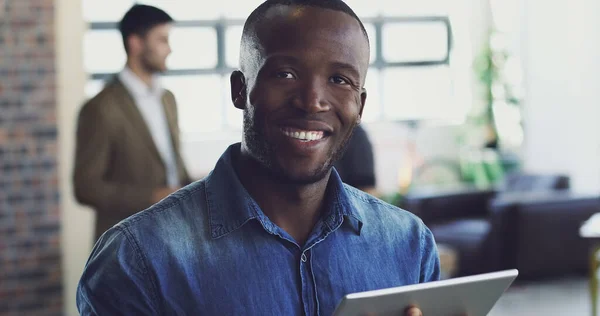 Positief succesvol. Gesneden portret van een knappe jonge zakenman aan het werk op zijn digitale tablet met een paar collega 's op de achtergrond. — Stockfoto