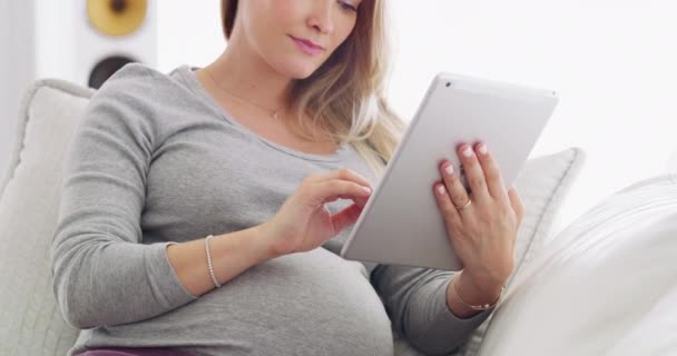 Dělám nějaký výzkum porodních technik. 4K video těhotné ženy pomocí svého digitálního tabletu při relaxaci na pohovce. — Stock video
