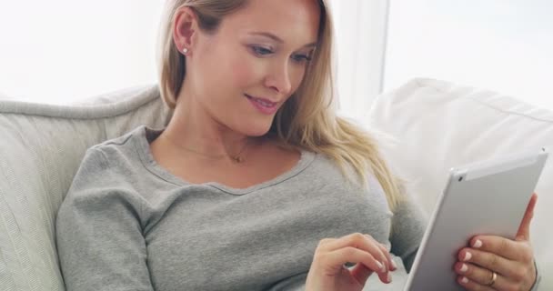 Er is zoveel te doen online. 4K beelden van een vrouw met behulp van haar digitale tablet terwijl ontspannen op haar bank thuis. — Stockvideo