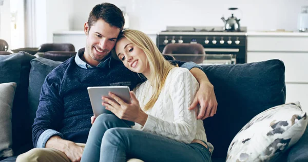 Navegando por la red juntos. Foto recortada de una pareja joven y cariñosa usando una tableta digital mientras están sentados en su sofá en casa. — Foto de Stock