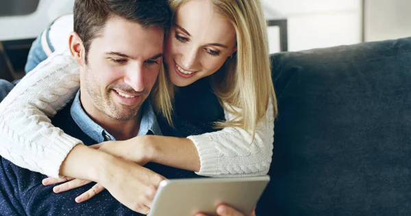 ¿Qué estás haciendo? Foto recortada de una pareja joven y cariñosa usando una tableta digital mientras están sentados en su sofá en casa. — Foto de Stock