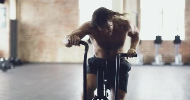 Elinden geleni yapıyor. Spor salonunda egzersiz bisikletinde çalışan kaslı bir gencin 4K videosu.. — Stok video
