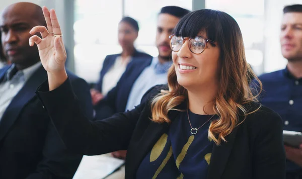 Me encantaría saber más. Fotografía de una joven empresaria sentada en la audiencia de una conferencia de negocios y levantando la mano. — Foto de Stock