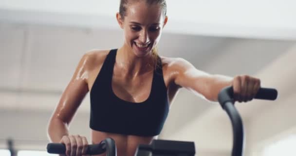 Schuppen kommen ins Schwitzen. 4k-Video einer attraktiven jungen Frau beim Training auf einem Heimtrainer im Fitnessstudio. — Stockvideo