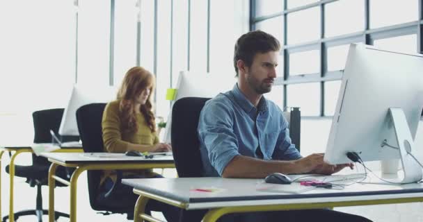 Begabte Designer bei der Arbeit. 4K-Videoaufnahmen eines jungen Designers, der an seinem Computer in einem modernen Büro arbeitet, mit Kollegen, die im Hintergrund arbeiten. — Stockvideo