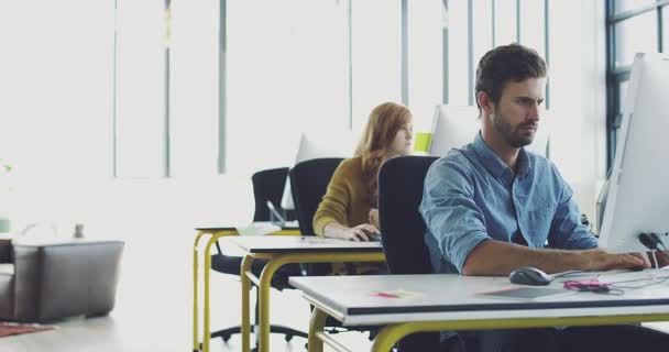 Enfocados en sus tareas de diseño. Imágenes de vídeo 4K de un joven diseñador trabajando en su ordenador en una oficina moderna con colegas trabajando en segundo plano. — Vídeos de Stock