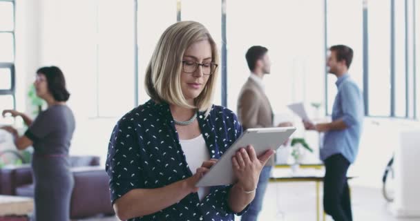 Wyróżnia się w biurze. Nagranie wideo 4K młodej kobiety korzystającej z tabletu cyfrowego, stojącej w nowoczesnym biurze ze współpracownikami w tle. — Wideo stockowe