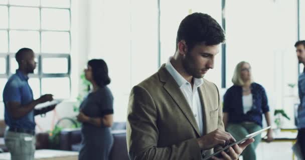 Sukces należy do mnie. Nagranie wideo 4K młodego mężczyzny korzystającego z tabletu cyfrowego, stojącego w nowoczesnym biurze ze współpracownikami w tle. — Wideo stockowe