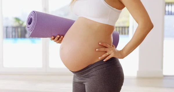 Elle montre sa bosse de bébé. Plan recadré d'une jeune femme enceinte méconnaissable portant un tapis de yoga. — Photo