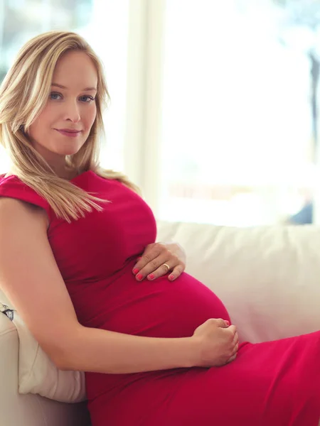 Zbliżamy się do randki. Portret atrakcyjnej, młodej kobiety w ciąży trzymającej brzuch podczas relaksu na kanapie w domu. — Zdjęcie stockowe