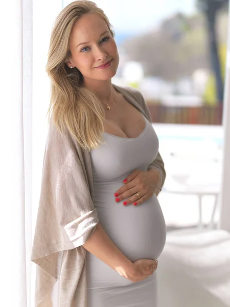 임신은 그녀에게 좋아 보 입니다. 집에서 있는 아름답고 임신 한 젊은 여자의 모습을 찍은 사진. — 스톡 사진