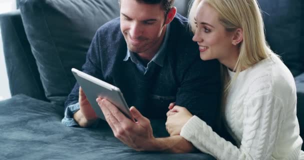 Komfort og tilslutningsmuligheder kombineret. 4K video optagelser af et kærligt ungt par ved hjælp af en digital tablet sammen på sofaen derhjemme. – Stock-video