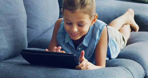 Po vyřešení školní zábavy. Snímek roztomilé holčičky pomocí digitálního tabletu na pohovce doma. — Stock fotografie