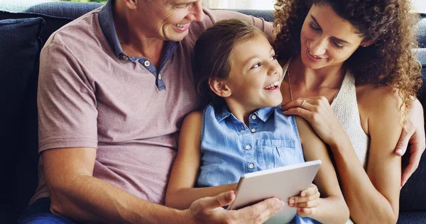 A TV é assim no ano passado, mãe. Tiro de uma menina bonita usando um tablet digital com sua mãe e pai no sofá em casa. — Fotografia de Stock