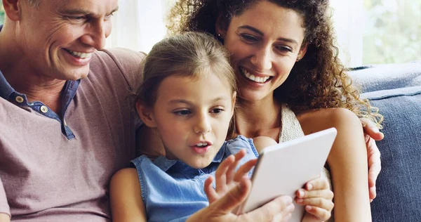 Familietijd tot een interactieve ervaring maken. Foto van een schattig klein meisje met behulp van een digitale tablet met haar moeder en vader op de bank thuis. — Stockfoto