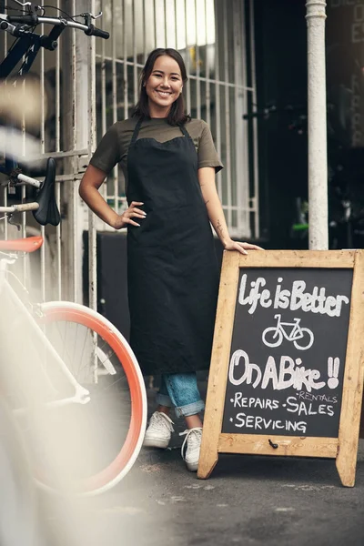 Entrez donc. Plan complet d'une jolie jeune femme debout devant son magasin de vélos pendant la journée. — Photo