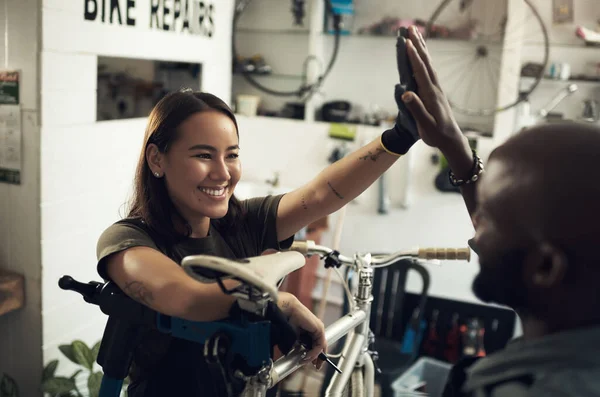 Buen trabajo con la pintura fresca. Disparo de dos jóvenes propietarios de negocios de pie juntos en su tienda de bicicletas y dándose unos a otros un máximo de cinco. — Foto de Stock