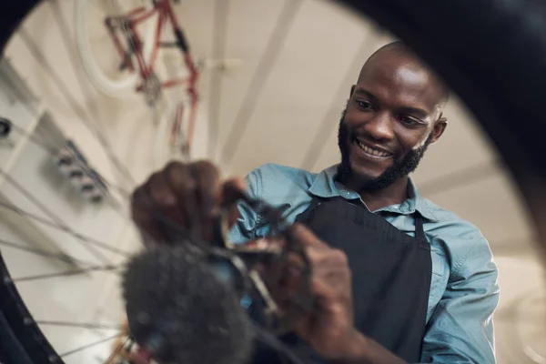 Esta moto realmente precisava de um novo papel. Baixo ângulo tiro de um jovem bonito de pé sozinho em sua loja e reparar uma roda de bicicleta. — Fotografia de Stock