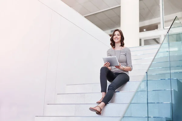 Bezprzewodowość to mądrzejsza droga do pracy. Portret młodej bizneswoman korzystającej z tabletu cyfrowego na schodach w nowoczesnym biurze. — Zdjęcie stockowe