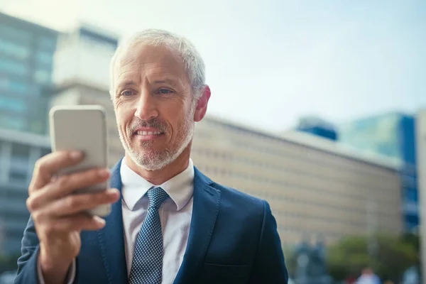 Dejando que sus dedos hablen. Fotografía de un hombre de negocios confiado usando su teléfono celular mientras estaba parado fuera de su edificio de oficinas. — Foto de Stock