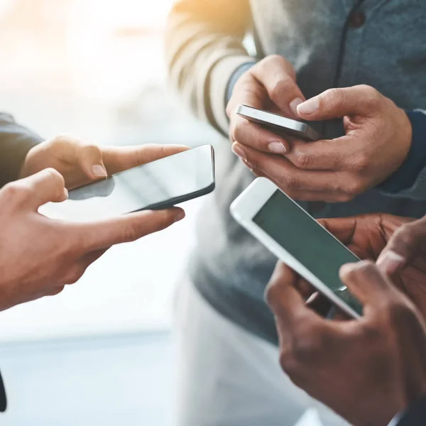 Es ist wichtig, in einer vernetzten Welt auf dem Laufenden zu bleiben. Aufnahme einer Gruppe unkenntlich gemachter Geschäftsleute mit ihren Mobiltelefonen im Büro. — Stockfoto