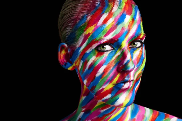 Kreatívak leszünk a színekkel. Stúdió lövés egy fiatal nő pózol élénk színű festék az arcán, szemben a fekete háttér. — Stock Fotó
