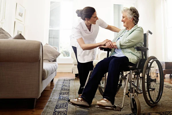 O melhor cuidado que podias esperar. Tiro de um cuidador sorridente ajudando uma mulher idosa em uma cadeira de rodas em casa. — Fotografia de Stock
