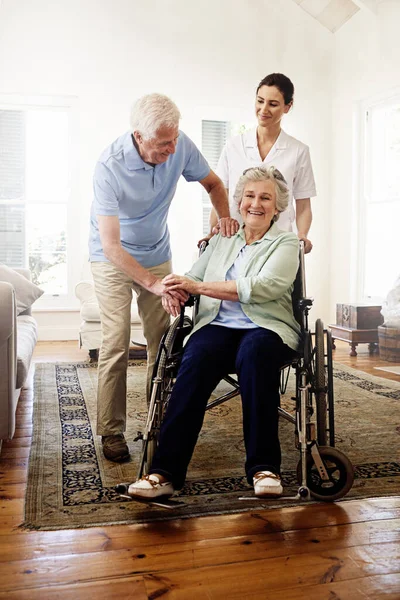 Оточений підтримкою. Постріл усміхненого доглядача з старшою жінкою в інвалідному візку та її чоловіка вдома . — стокове фото