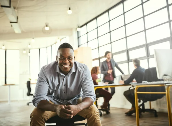 Er is niets beter dan een ontwerper te zijn. Gesneden portret van een knappe jonge zakenman zittend in het kantoor met zijn collega 's op de achtergrond. — Stockfoto