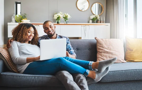 Der Komfort des Couchsurfens. Aufnahme eines jungen Paares, das es sich zu Hause auf dem Sofa gemütlich macht und gemeinsam einen Laptop benutzt. — Stockfoto