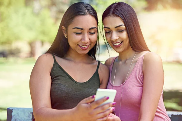 Verificar o mais recente zumbido nas redes sociais. Tiro cortado de dois jovens amigos usando um celular fora. — Fotografia de Stock