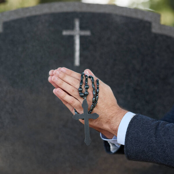 Praying for eternal peace. Cropped shot of a man praying with a rosary at a gravesite.